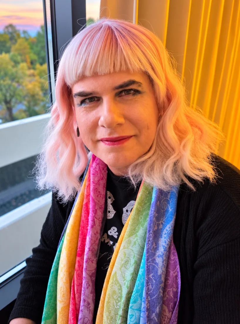 Portrait of Erika X. Driscoll wearing a rainbow scarf beside a window